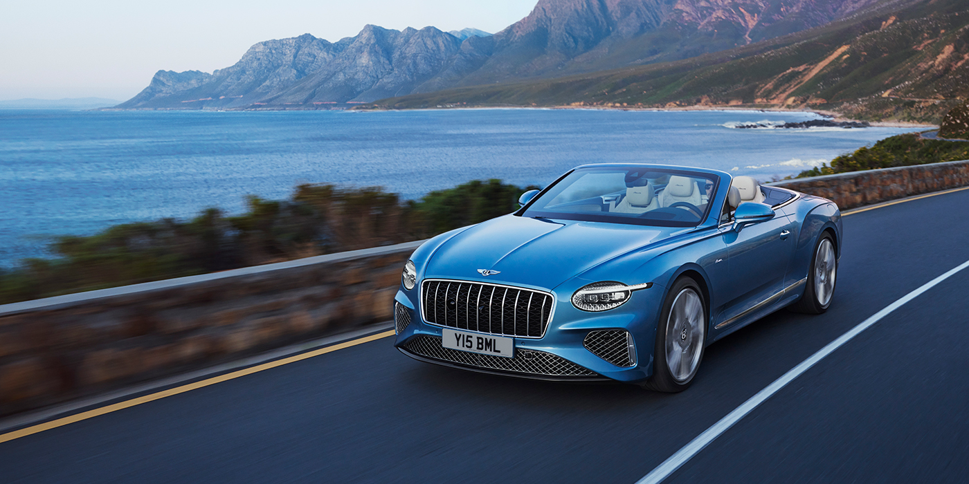 Bentley Lisboa New Bentley Continental GTC Azure convertible in Light Windsor blue paint with 22 inch Azure wheels and chrome grill, driving dynamically by the sea