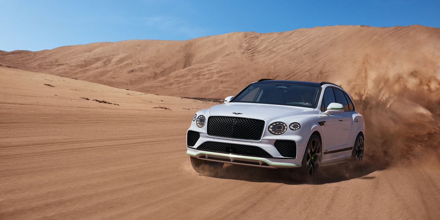 Bentley Lisboa Bentley Bentayga Speed SUV front three quarter in Snow Quarts Pearlescent by Mulliner white paint driving dynamically through the desert