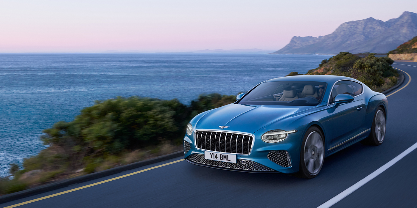 Bentley Lisboa New Bentley Continental GT Azure coupe in Light Windsor blue paint with 22 inch Azure wheels and chrome grill, driving dynamically by the sea