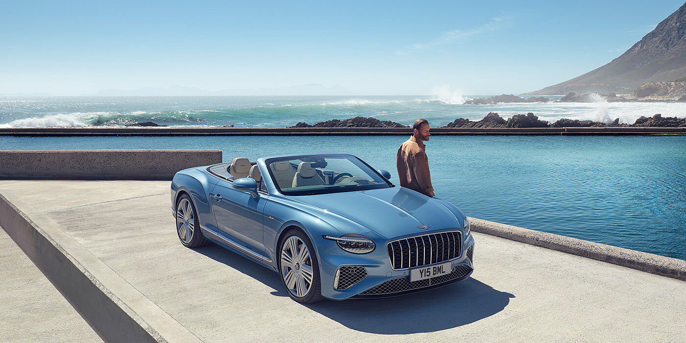 Bentley Lisboa New Bentley Continental GTC Azure convertible front view in Light Windsor blue paint with 22 inch ten spoke wheels parked by the sea in the sunshine