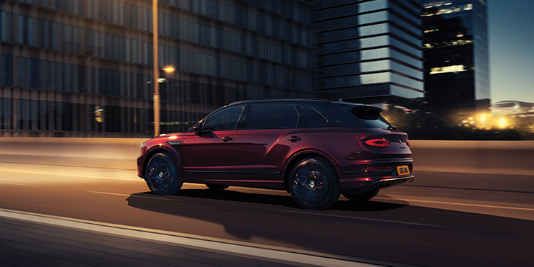 Bentley Lisboa Bentley Bentayga Extended Wheelbase Mulliner SUV in Cricket Ball red paint driving dynamically in city at night